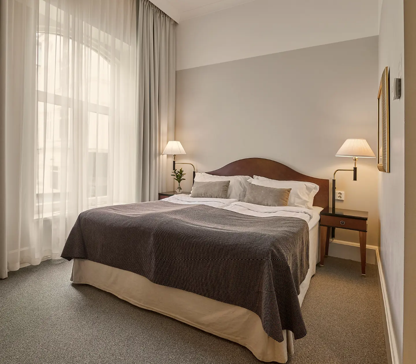 Cozy hotel room with twin beds featuring red patterned headboards, white bedding, and red accent pillows. Modern bedside tables with glass lamps add elegance.