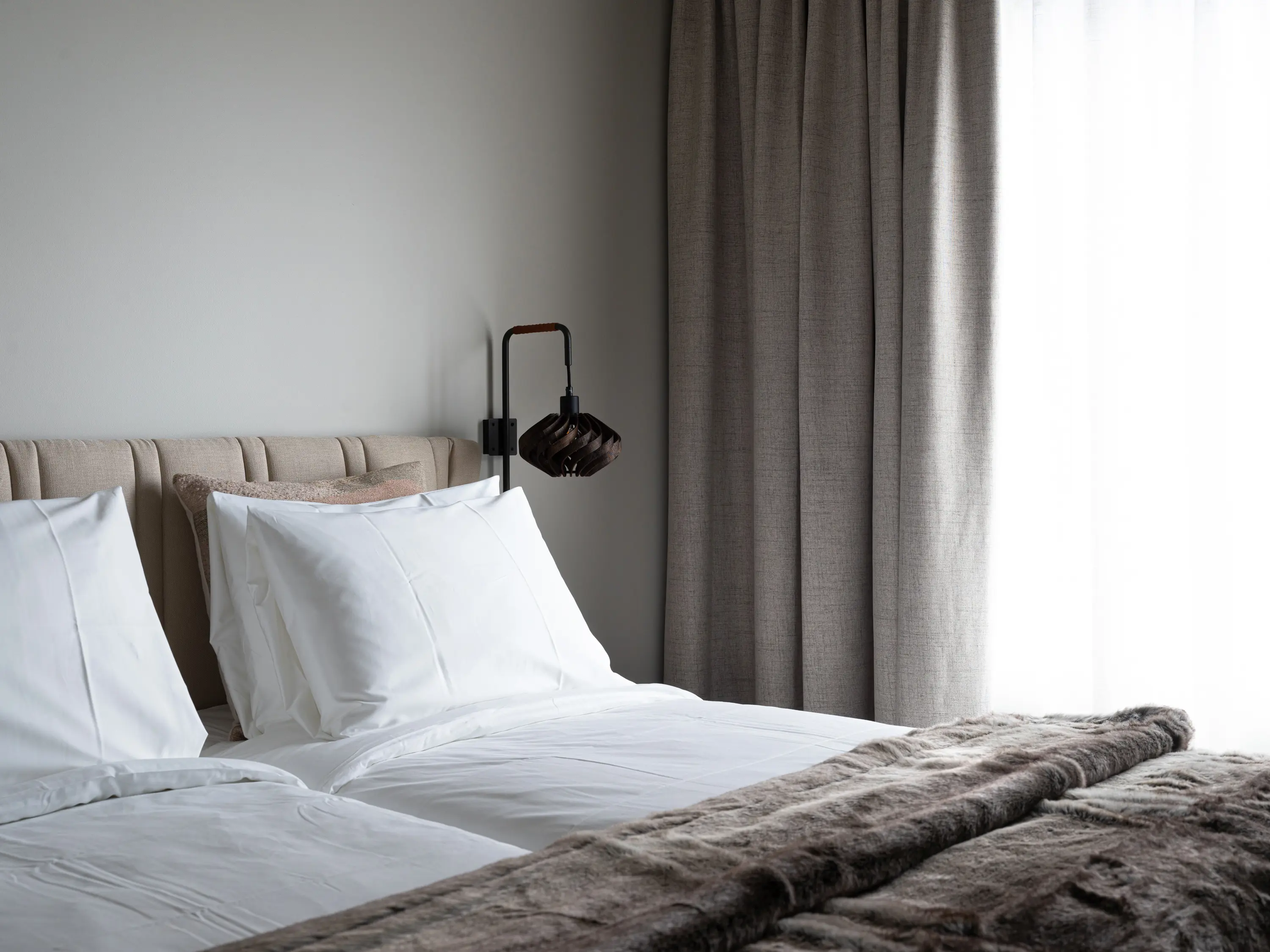 Close-up of a made bed with white sheets and a faux fur throw.