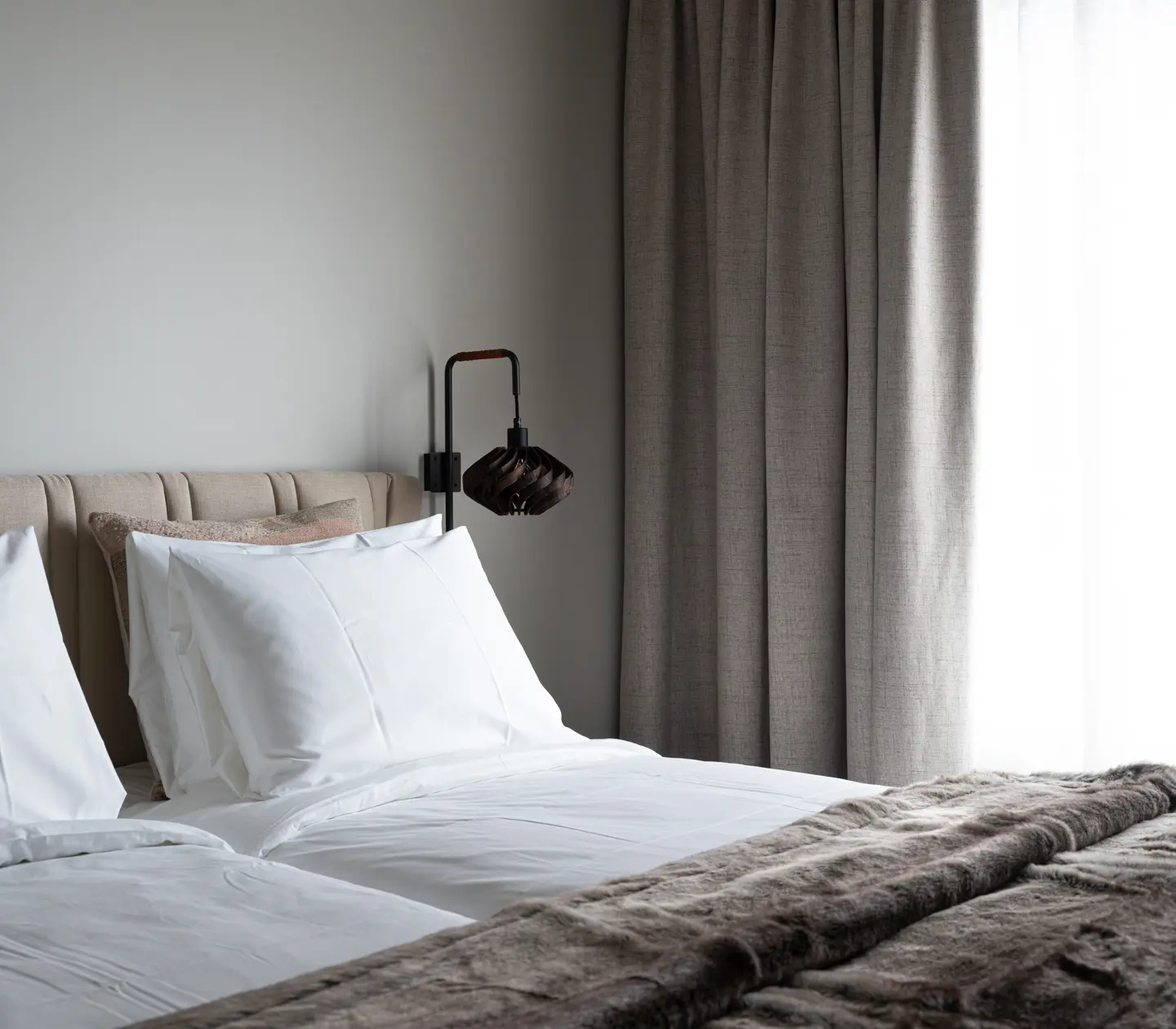 Close-up of a made bed with white sheets and a faux fur throw.