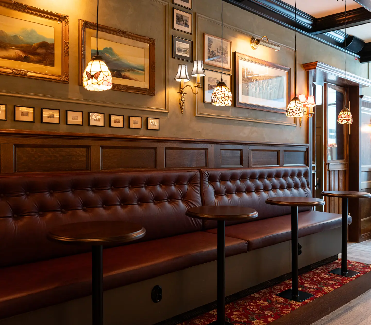 Seats along a wall in dark leather with small bar tables at Bishop Arms