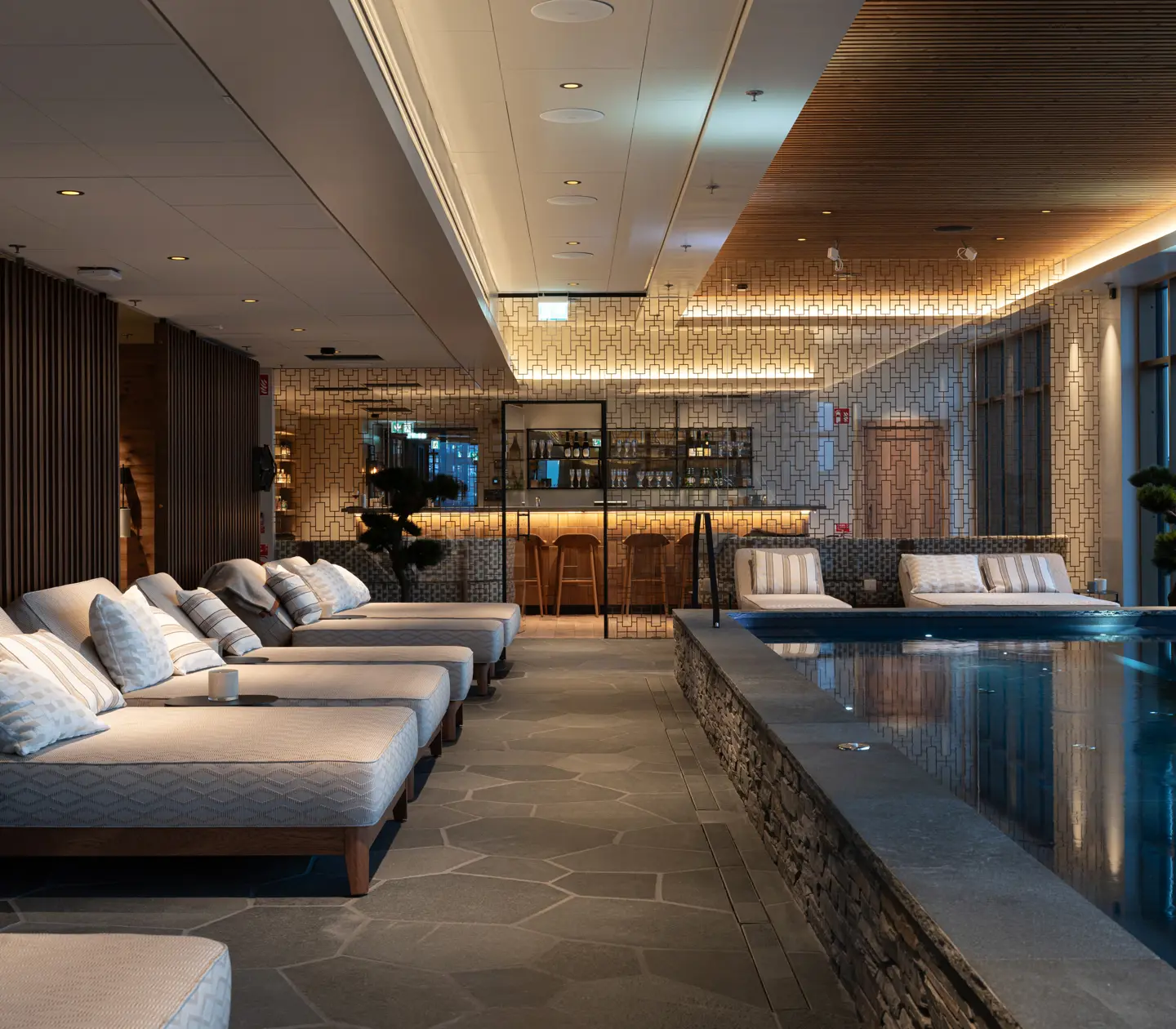 Wide view of Vana Spa in Kiruna with a pool, sun loungers, and dark grey stone flooring.