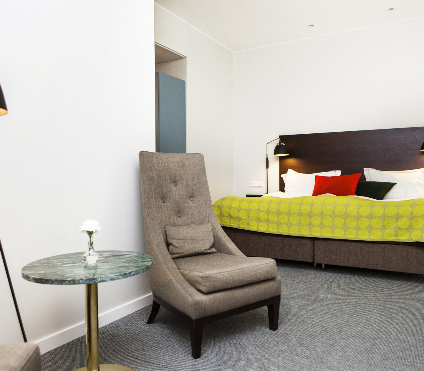 Ljust hotellrum med säng, fåtölj och lampa