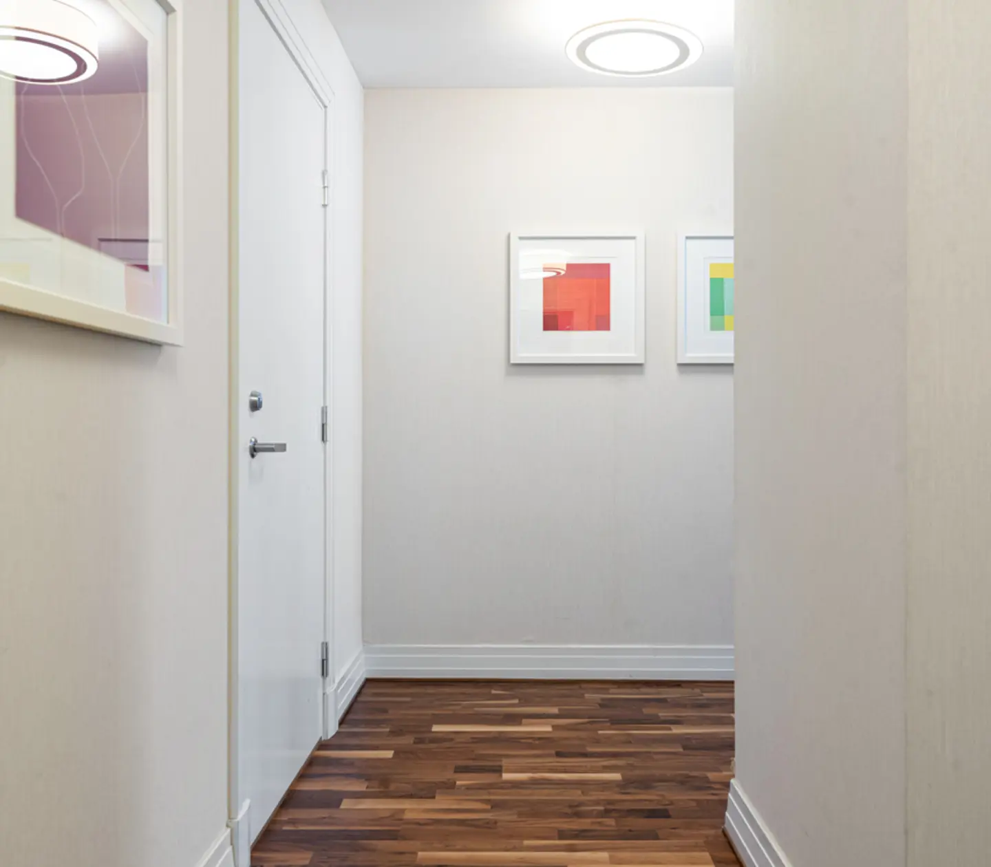 Modern hallway with wooden flooring, white walls, and framed abstract artwork on the walls.