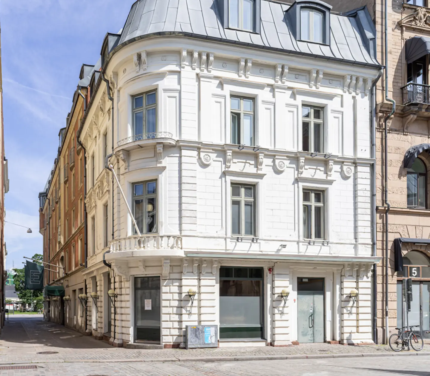 Vit historisk byggnad i centrala Stockholm med dekorativa detaljer och fönster på flera våningar, en solig dag med klarblå himmel.