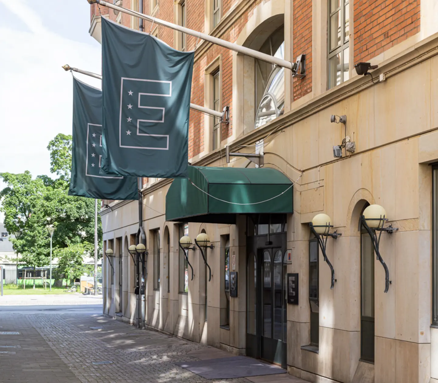 Fasad av anrikt hotell i stadsmiljö med gröna flaggor och entré med markis.