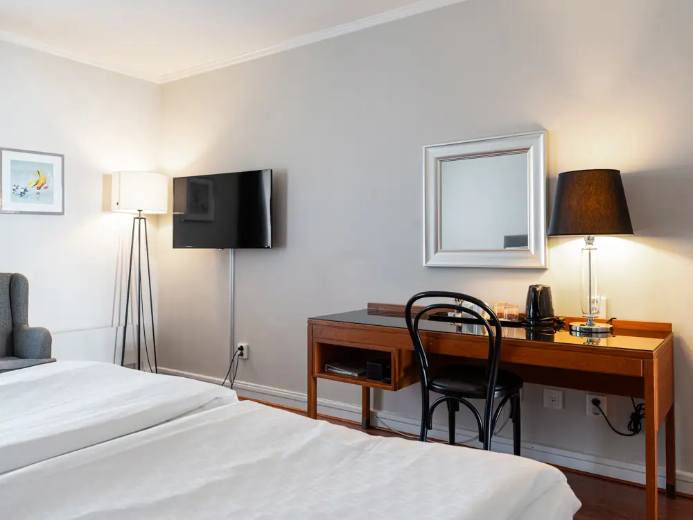 Modernt hotellrum med en dubbelsäng, skrivbord, platt-TV och stående lampa.