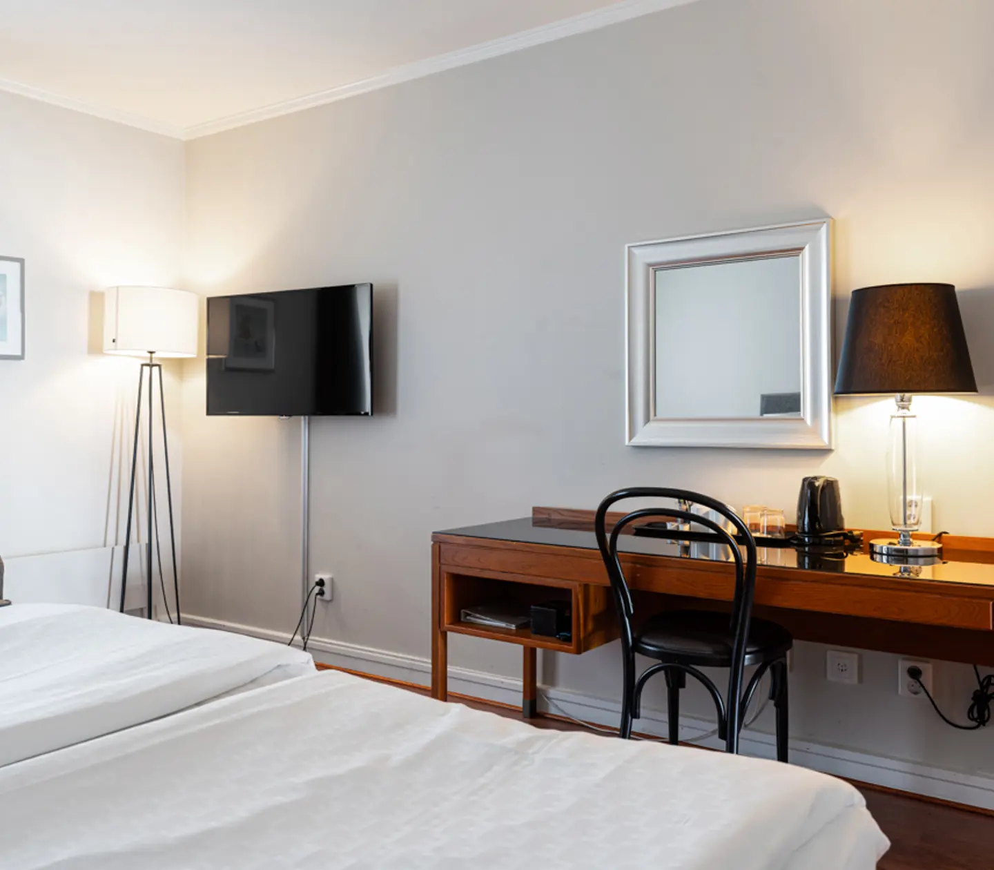 Modernt hotellrum med en dubbelsäng, skrivbord, platt-TV och stående lampa.