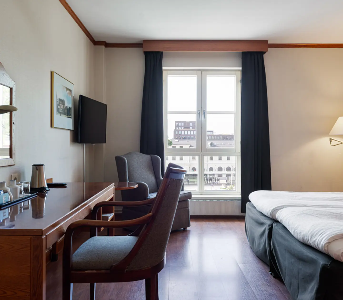 Modernt hotellrum med dubbelsäng, skrivbord, fåtölj och utsikt genom ett stort fönster.