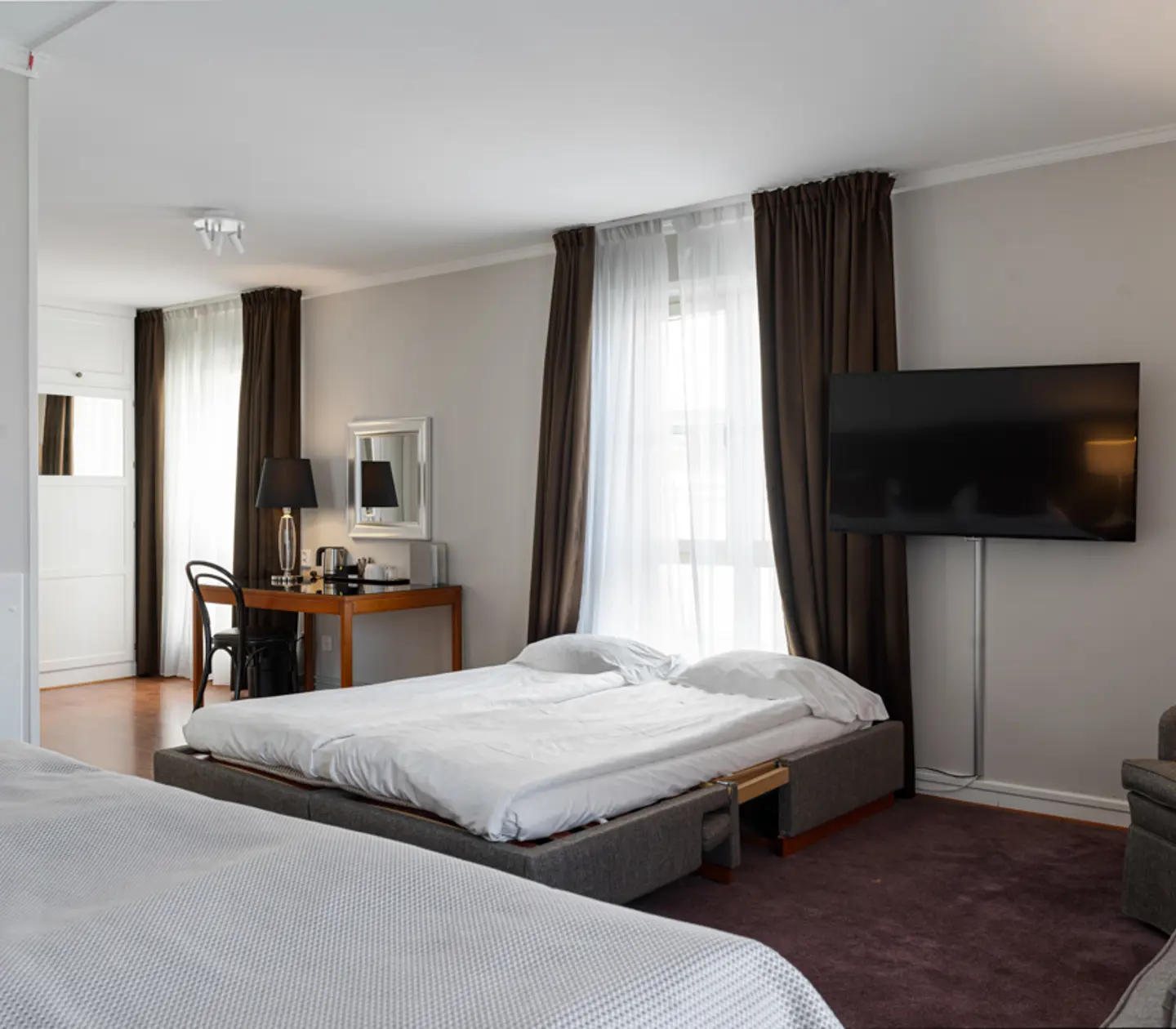 Modernt hotellrum med dubbelsäng, arbetshörna, stor TV och sittgrupp.