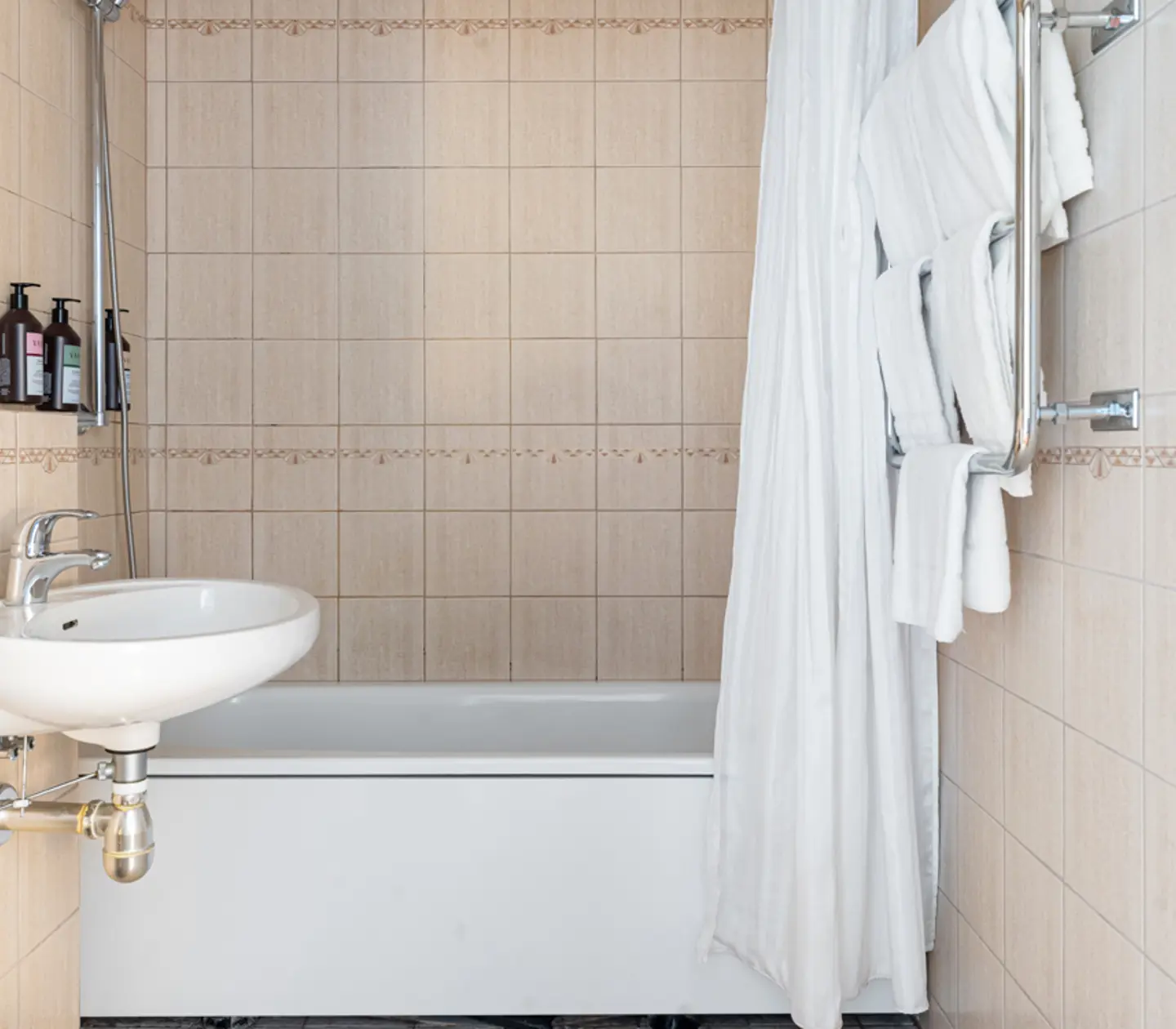 Modernt badrum med beige kakel, vit handfat, och vit badkar med duschdraperi.