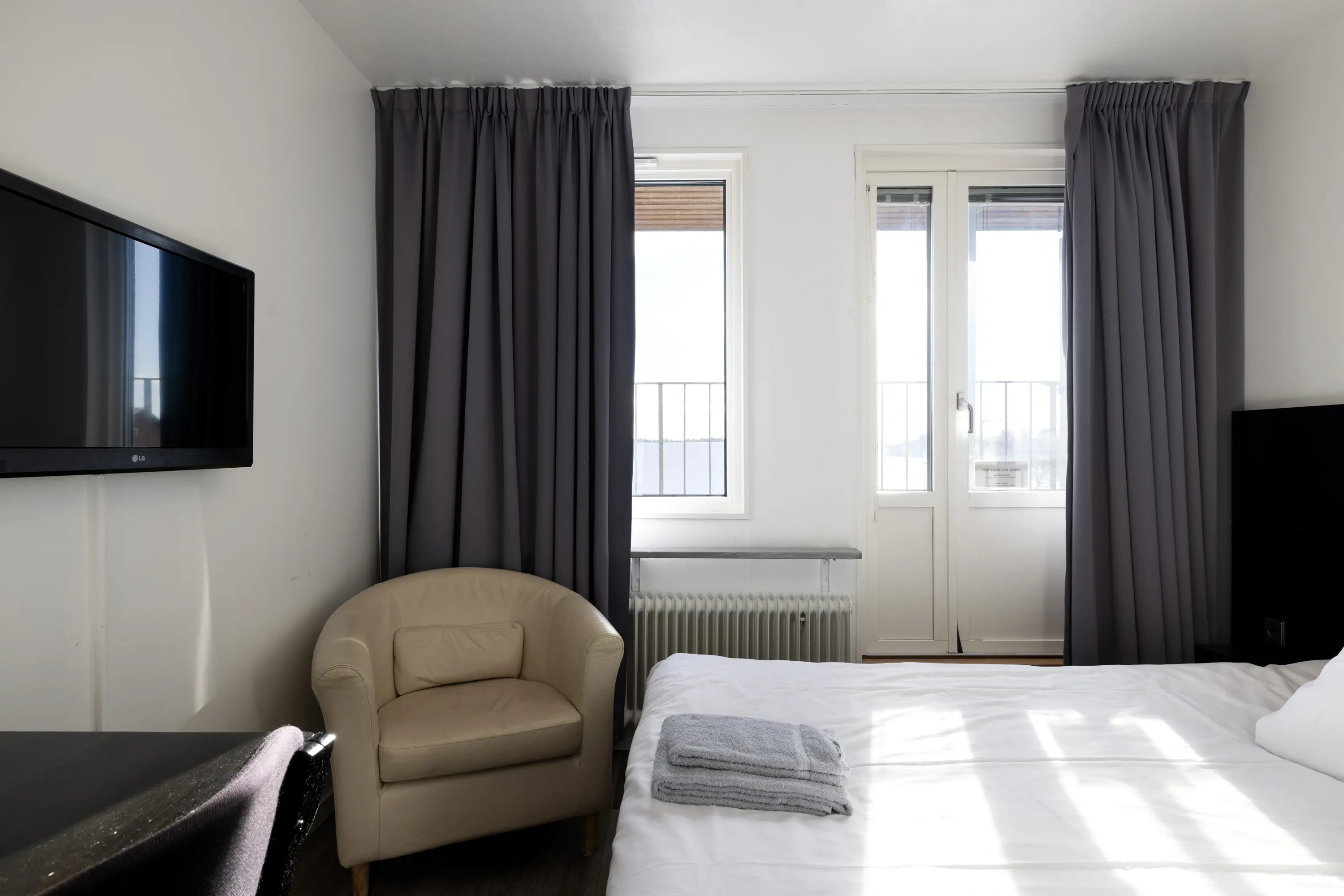 Hotel room with bed, beige leather armchair and TV