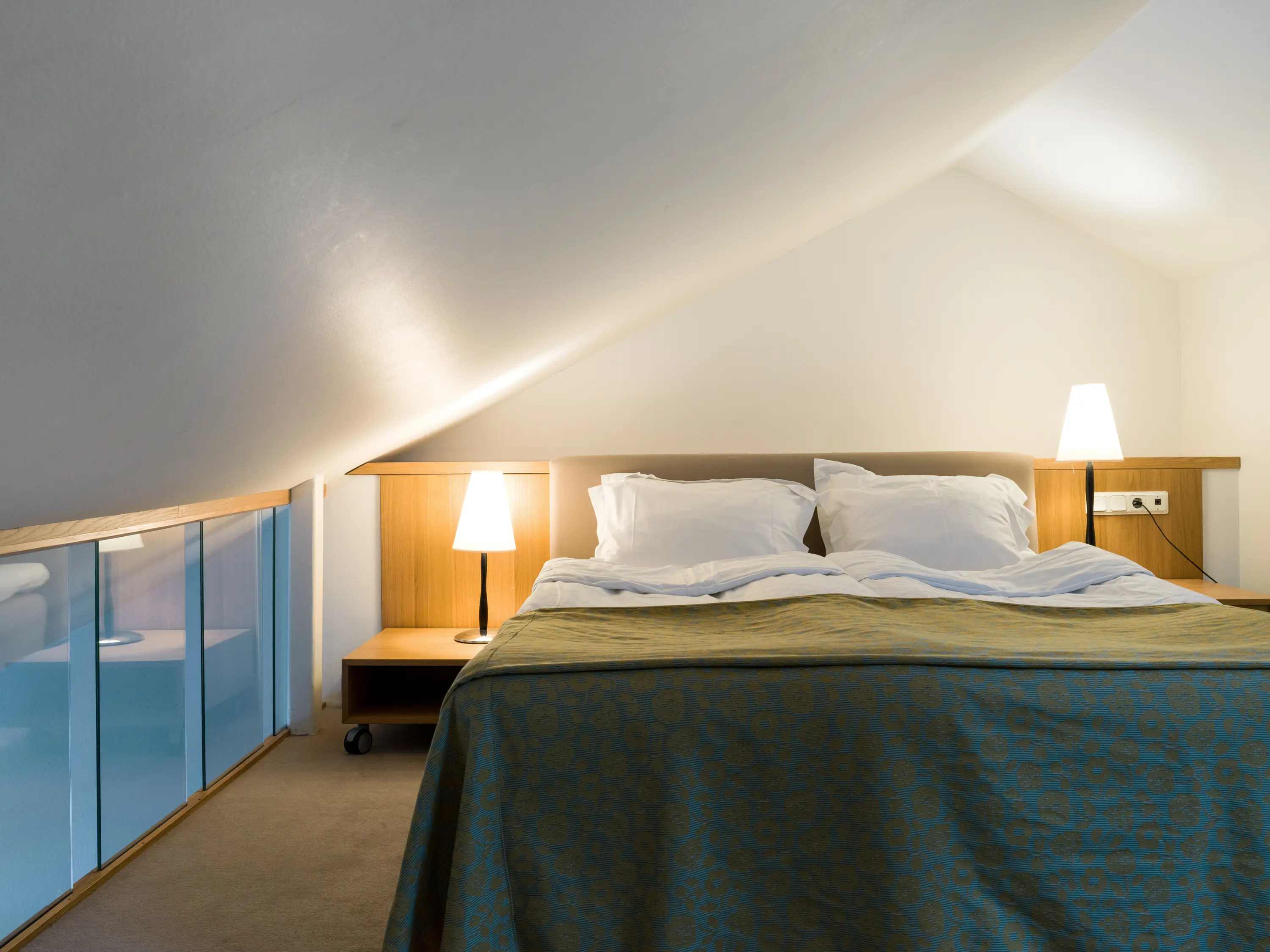 Bright hotel room with bed, glass railing and bedside lamps