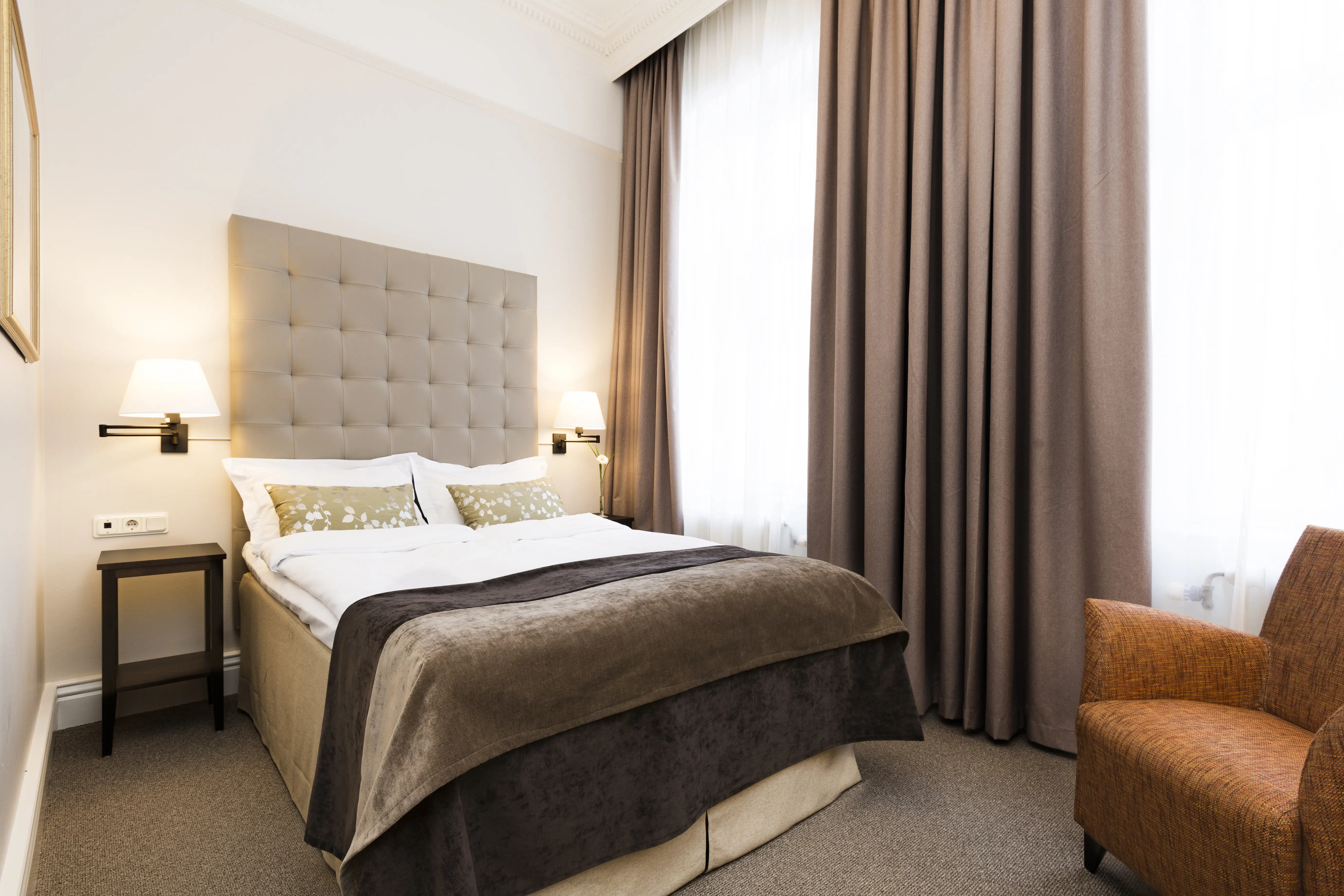 Bright hotel room with bed, gray headboard and armchair