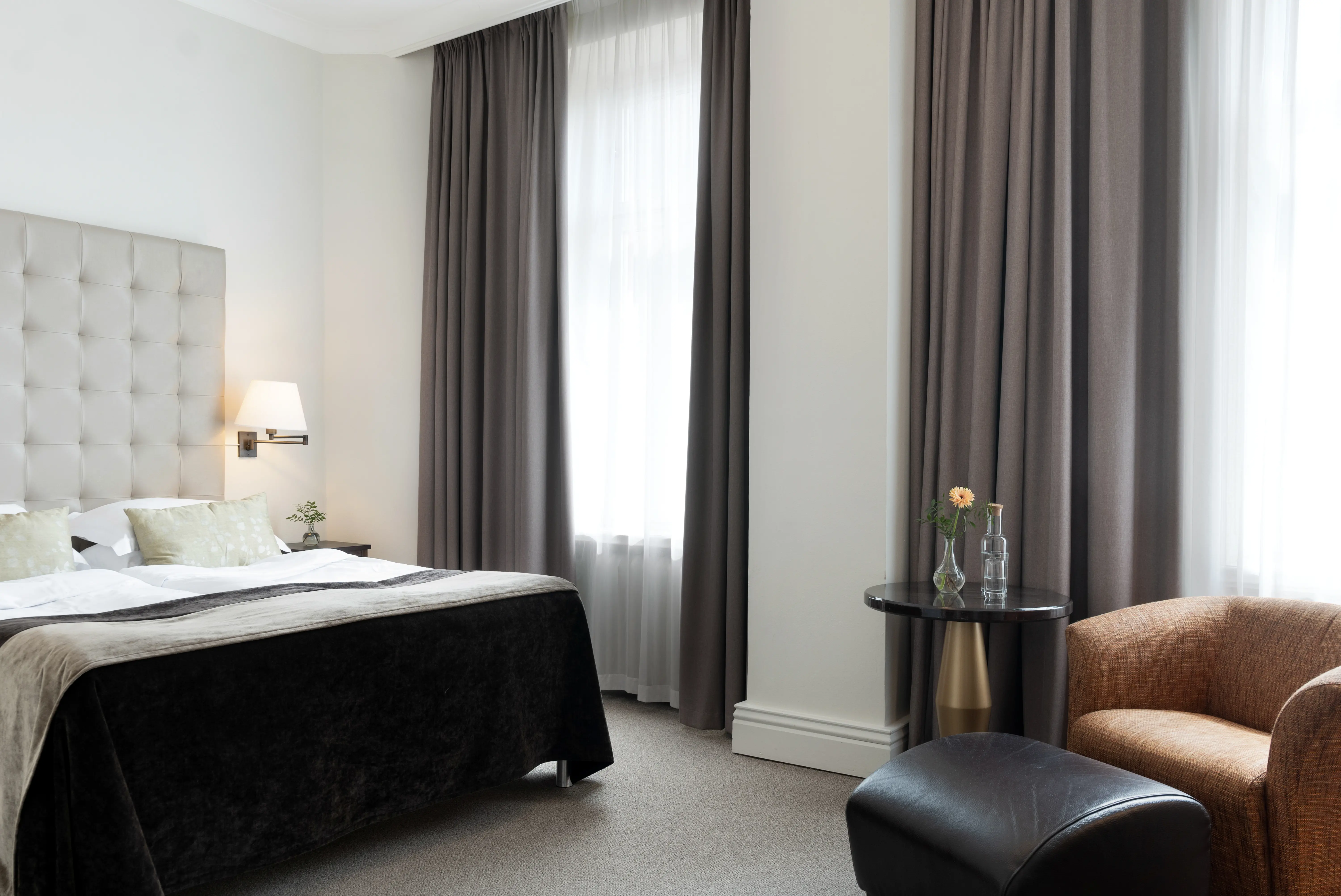 Bright hotel room with bed, white headboard and armchairs