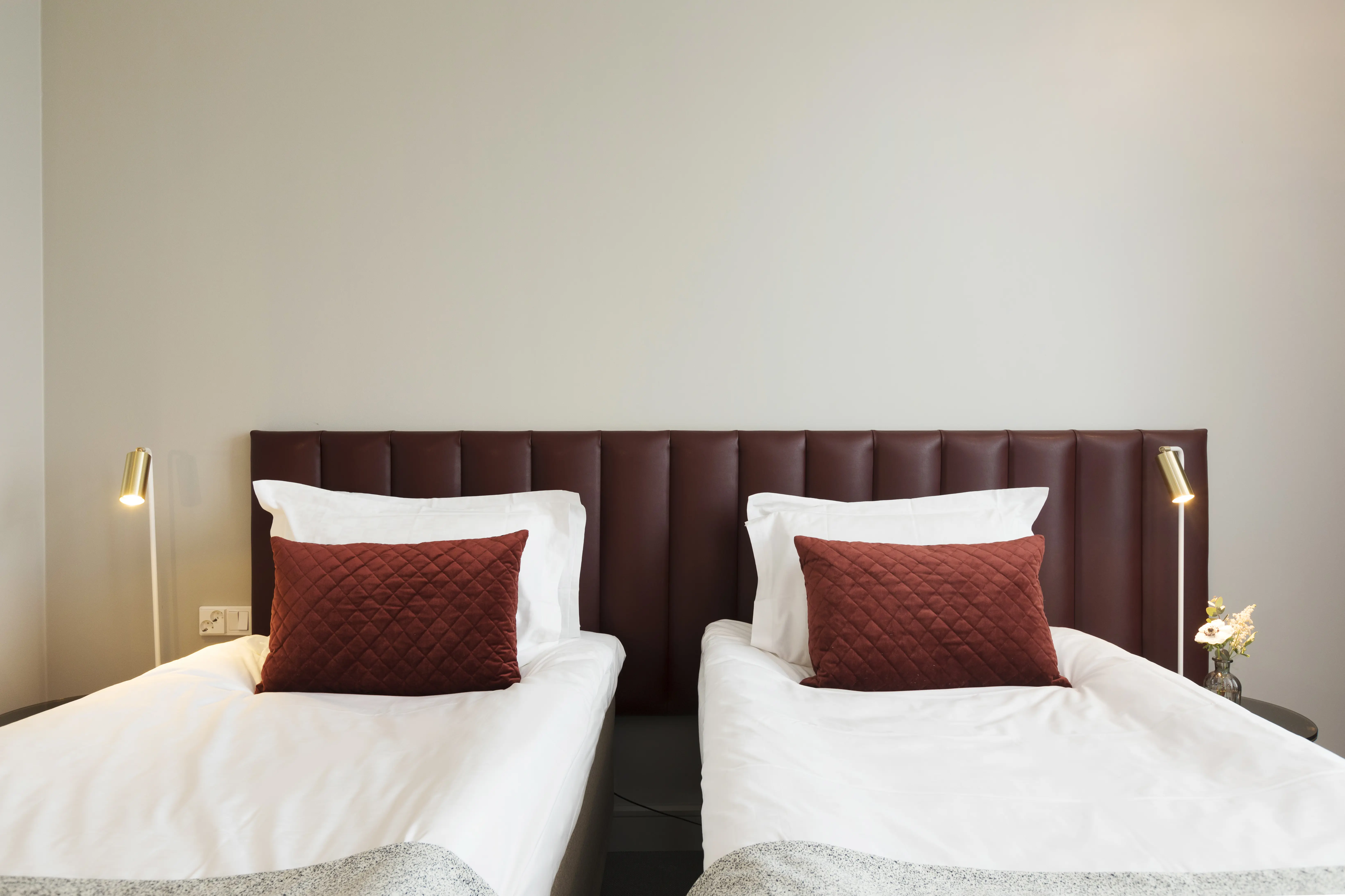 Bright hotel room with two single beds next to each other, burgundy headboard and small bedside lamps