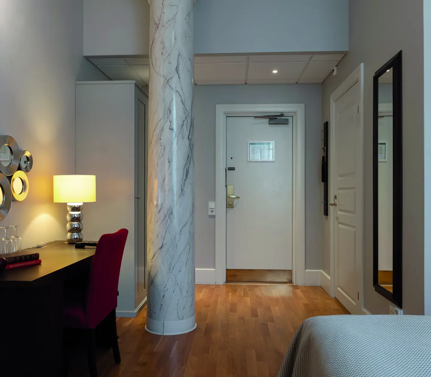 Modern hotellrum med arbetsplats, marmorpelare, vita väggar och trälaminatgolv.