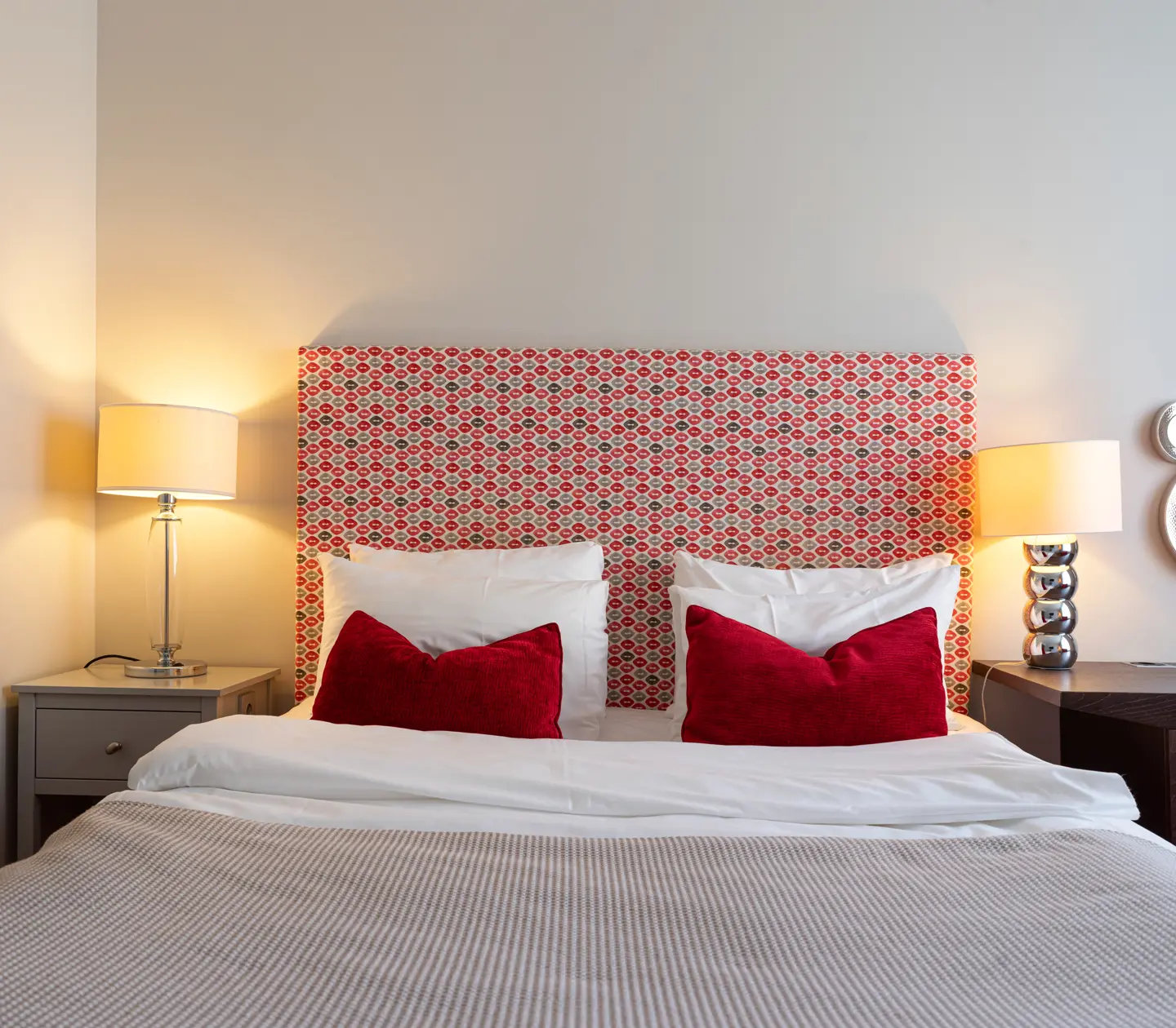 Hotellrum med säng, nattduksbord och rödmönstrad sänggavel