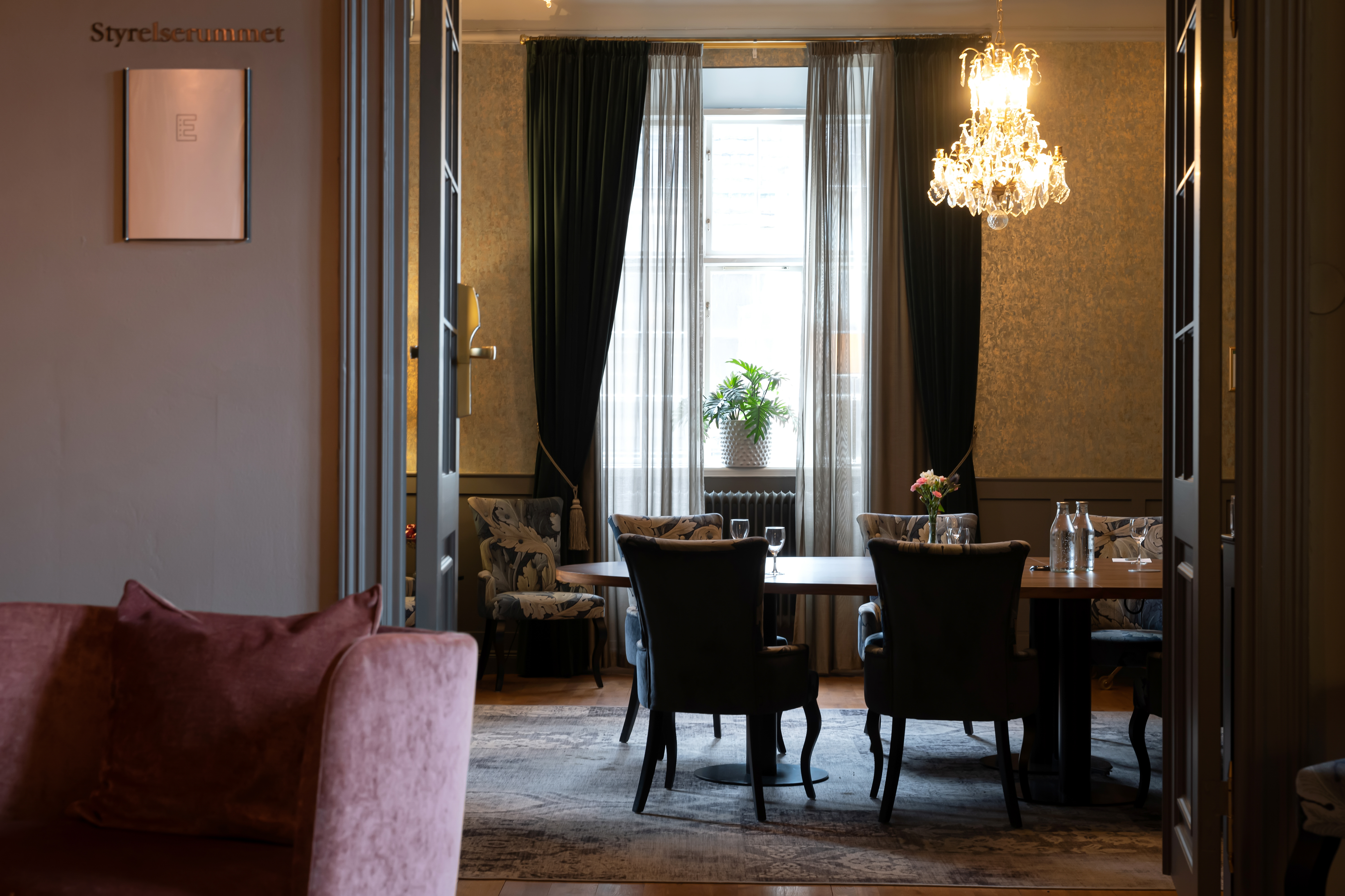 Open door to conference room with round table, window and crystal chandelier