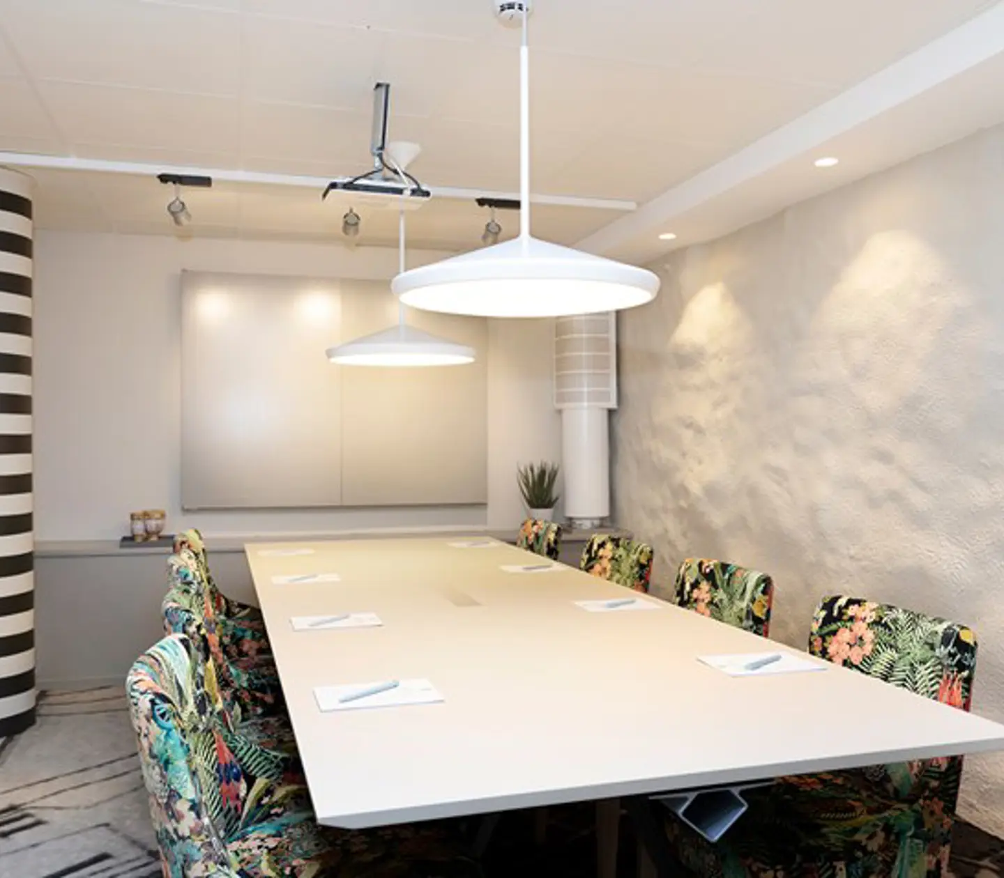 Conference room with board seating, white table, white walls and patterned chairs